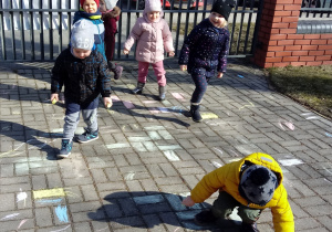 Dzieci malują kolorowymi kredami płyty chodnika przy przedszkolu